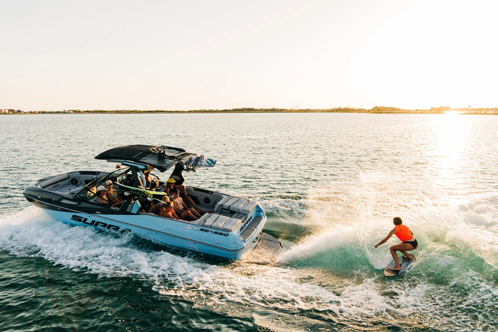 Wakesurfer riding behind a Supra boat at sunset