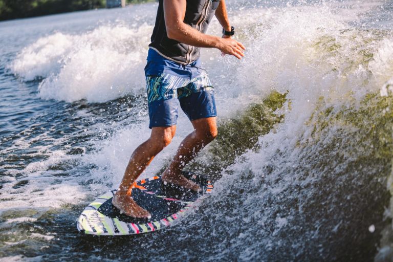 Active wakesurfer jumping on wake board down the river waves. Surfer on wave. Male athlete training on wakesurf training. Active water sports in open air on board. A man catches a wave on surf.