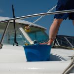 Man washing white boat with brush and pressure water system at pier. Yacht maintenance concept.